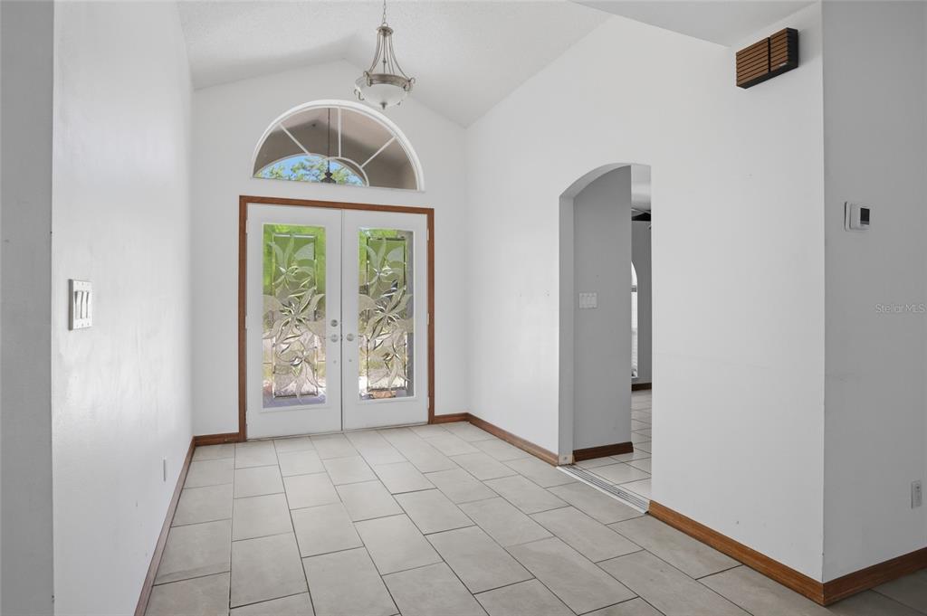 An entryway with white walls, tile flooring, a vaulted ceiling, and double glass-paneled front doors — 112 AUGUSTA CIRCLE, ST CLOUD, FL
