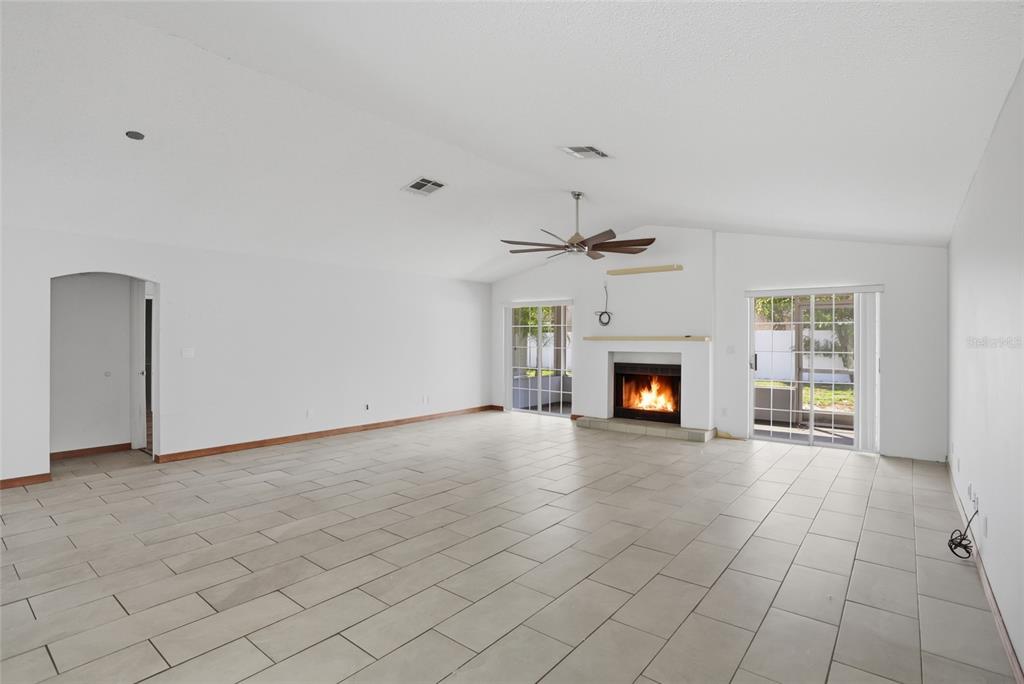 A spacious living room with white walls, tile flooring, a fireplace, and sliding glass doors — 112 AUGUSTA CIRCLE, ST CLOUD, FL