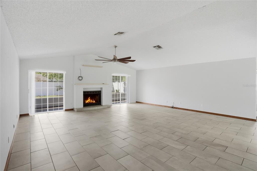 A spacious living room with white walls, tile flooring, a fireplace, and sliding glass doors — 112 AUGUSTA CIRCLE, ST CLOUD, FL