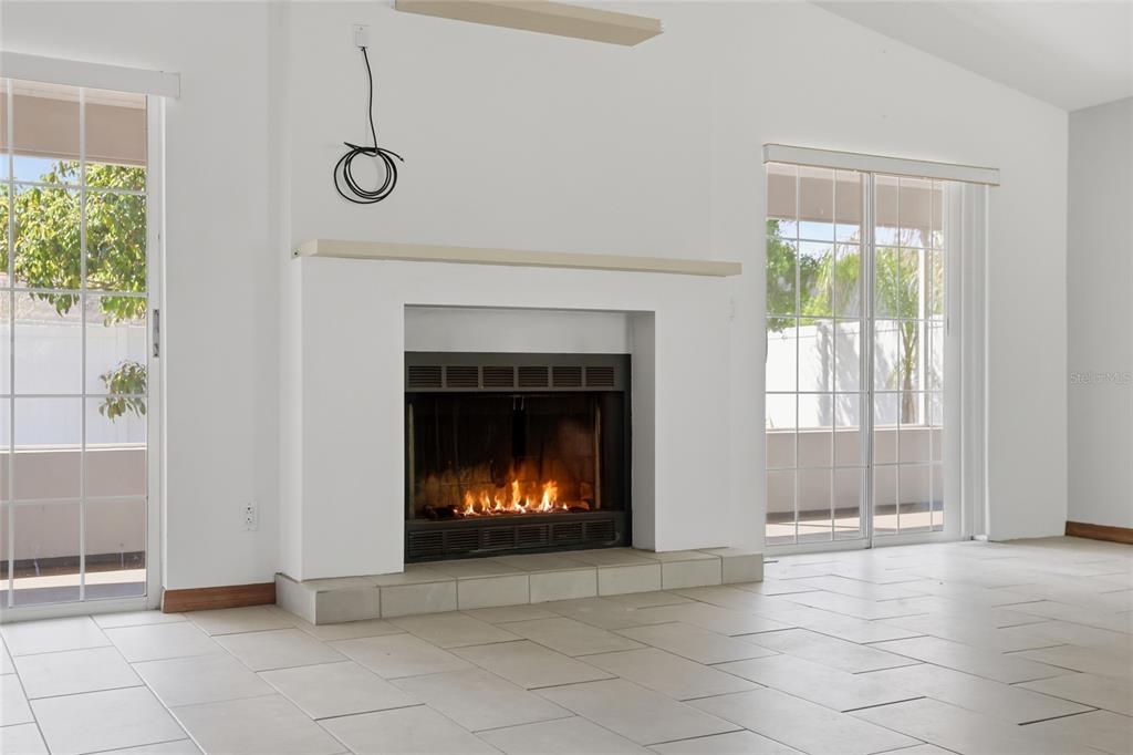 A living room features a white fireplace, tile flooring, and sliding glass doors on both sides — 112 AUGUSTA CIRCLE, ST CLOUD, FL