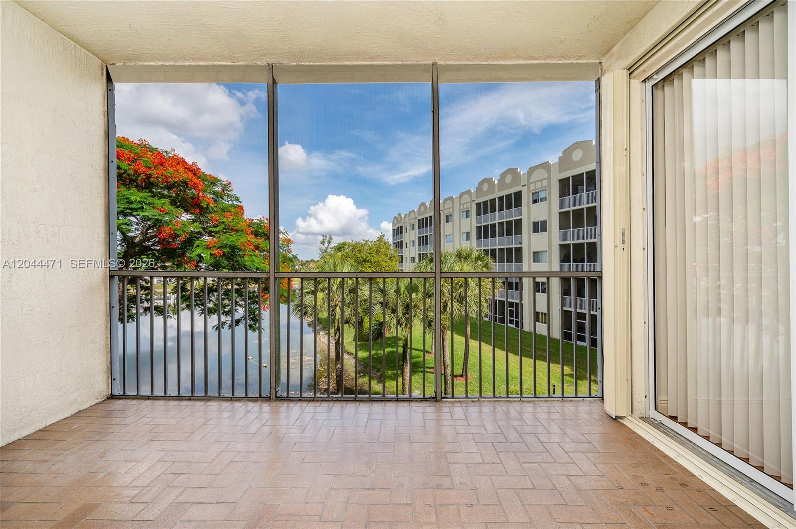 A screened-in balcony features tiled flooring, a metal railing, and a view of a lake — 10750 NW 66th St # 312, Doral FL 33178, DORAL, FL