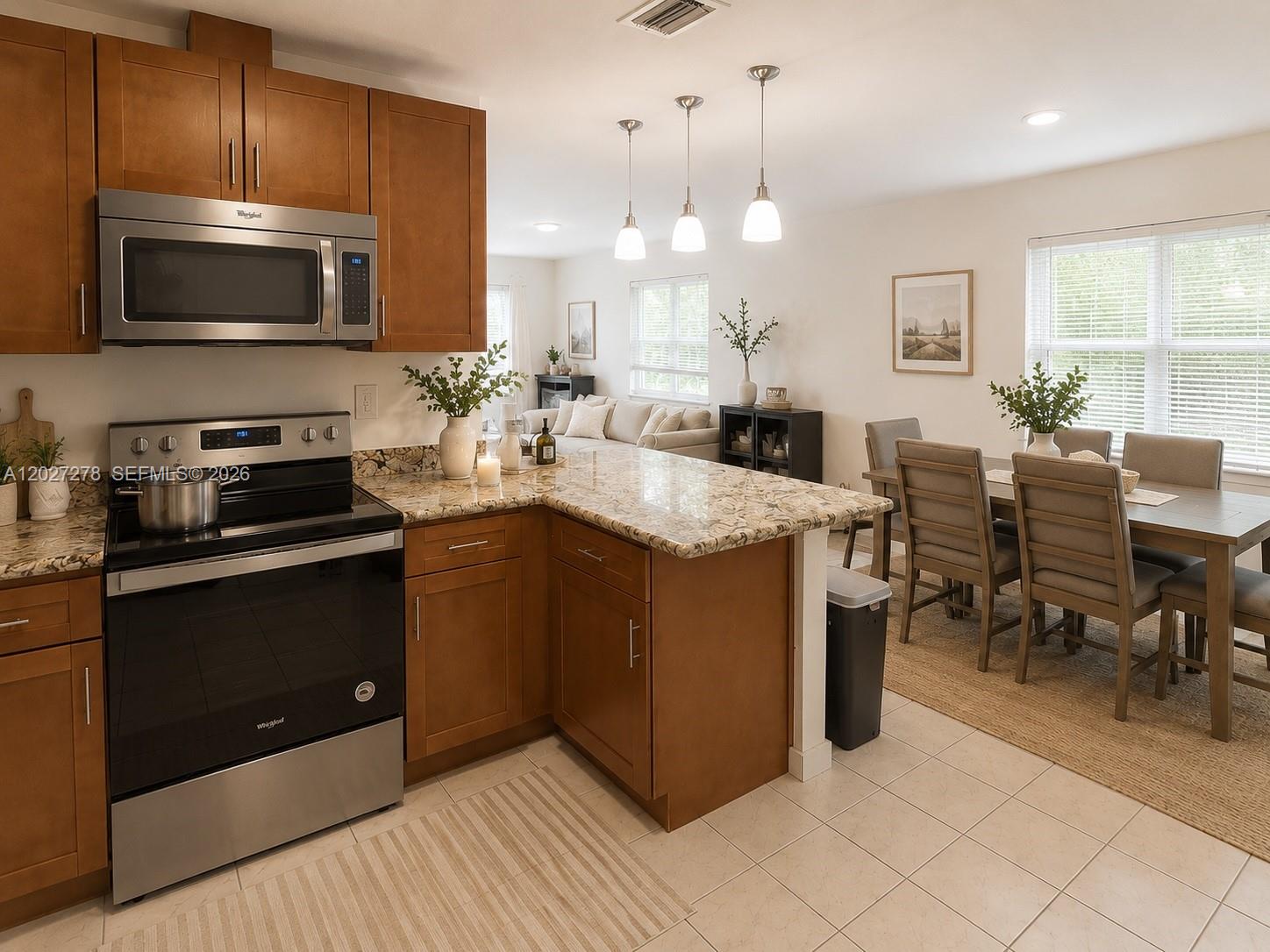 A kitchen with wood cabinets and granite countertops opens into a dining and living area — 901 NE 2nd St, Hallandale Beach FL 33009, HALLANDALE BEACH, FL