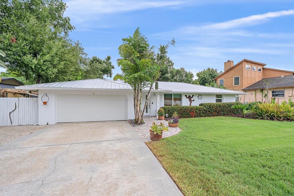 A single-story white house with a metal roof, a two-car garage, and a landscaped lawn — 4271 LAGO WAY, SARASOTA, FL