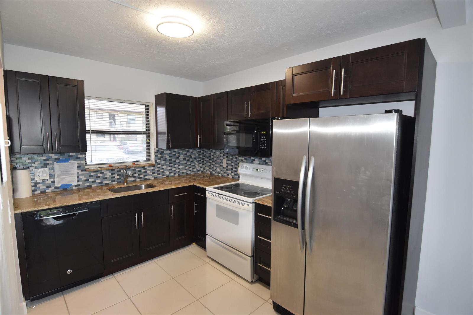 A kitchen with dark wood cabinets, stainless steel appliances, a white stove, and tile backsplash — 21895 Lake Forest Circle # 102, Boca Raton FL 33433, BOCA RATON, FL