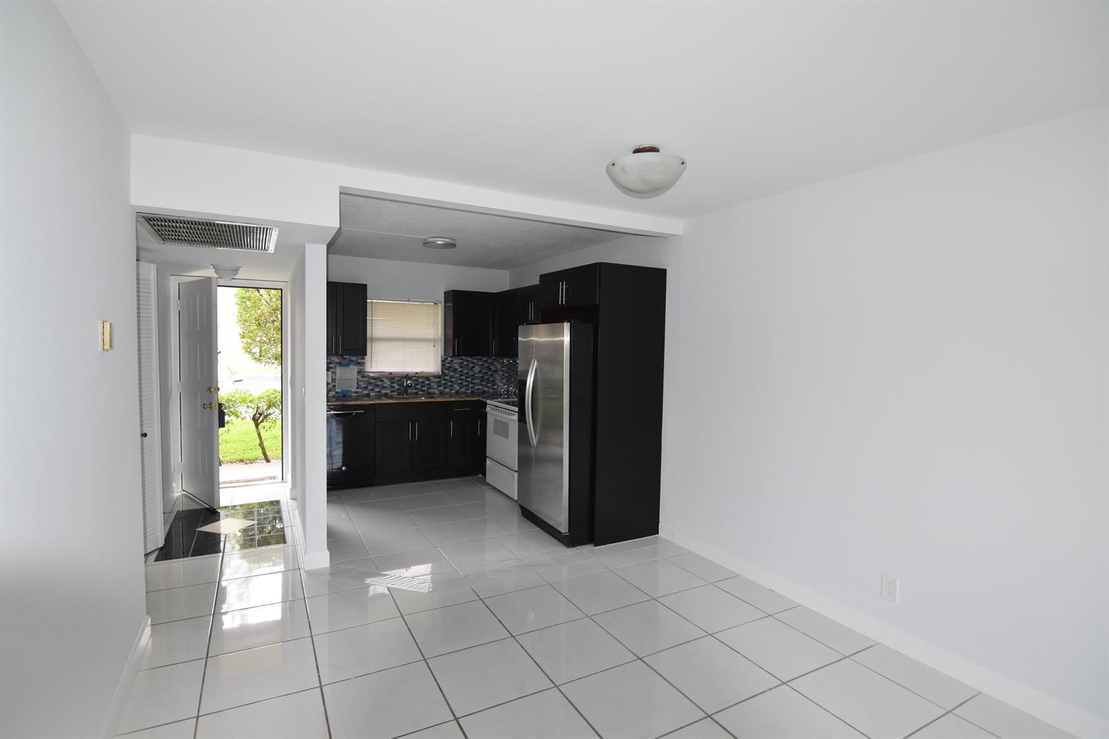 A kitchen with dark cabinets and stainless steel appliances opens to a tiled living area — 21895 Lake Forest Circle # 102, Boca Raton FL 33433, BOCA RATON, FL