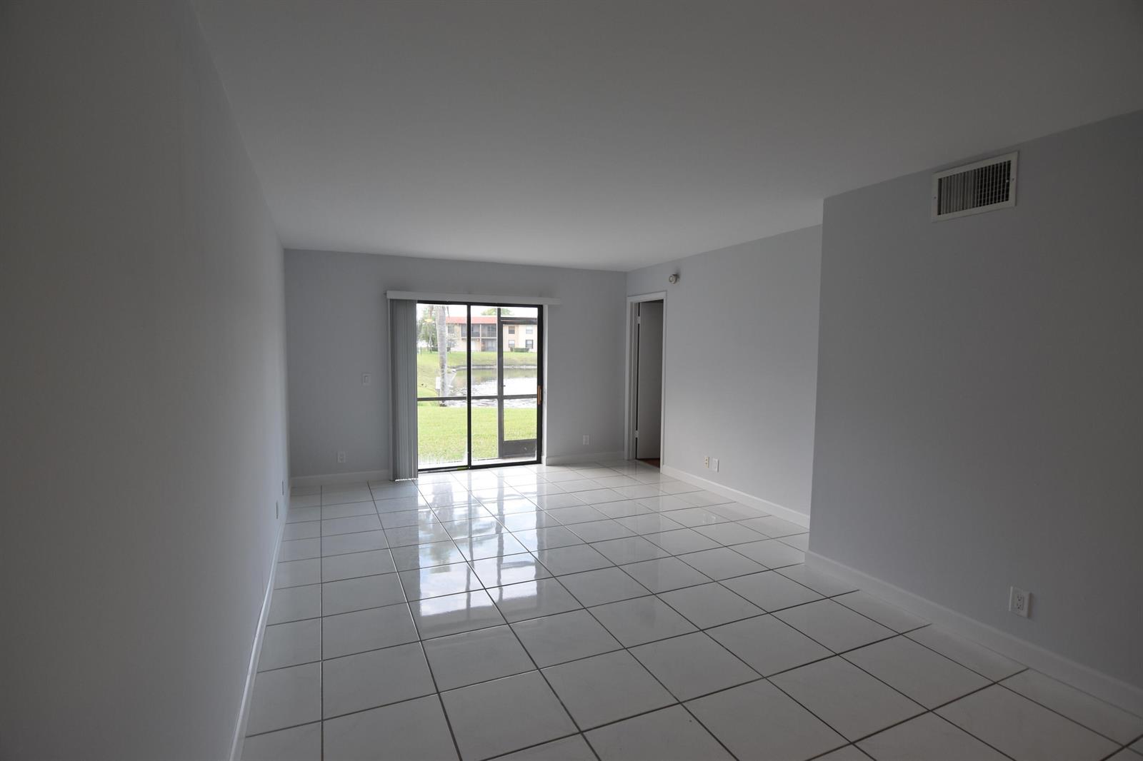 An empty living room features white tile flooring, light gray walls, and a sliding glass door — 21895 Lake Forest Circle # 102, Boca Raton FL 33433, BOCA RATON, FL