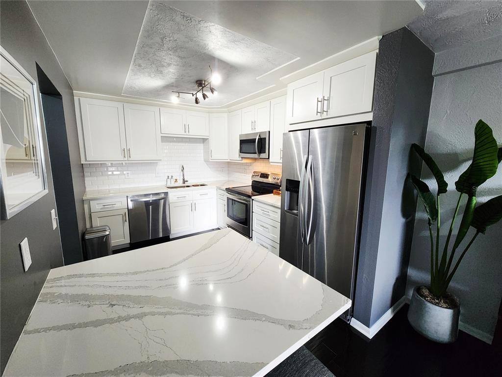 A modern kitchen features white cabinets, stainless steel appliances, and a white quartz island countertop — 4651 1ST STREET NE UNIT 306, ST PETERSBURG, FL