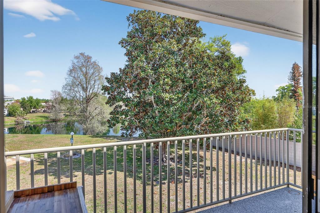 A balcony with a metal railing overlooks a grassy yard, a large tree, and water — 1935 CONWAY ROAD UNIT F6, ORLANDO, FL