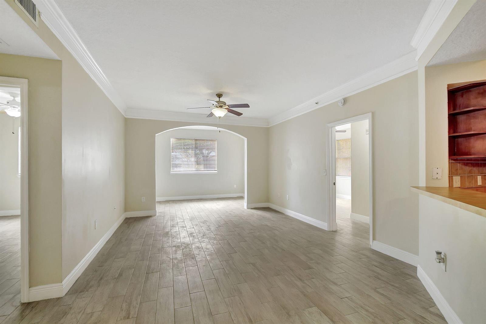 An empty living area features light-colored wood-look tile flooring, an arched entryway, and a ceiling fan — 9849 Baywinds Drive # 8101, West Palm Beach FL 33411, WEST PALM BEACH, FL