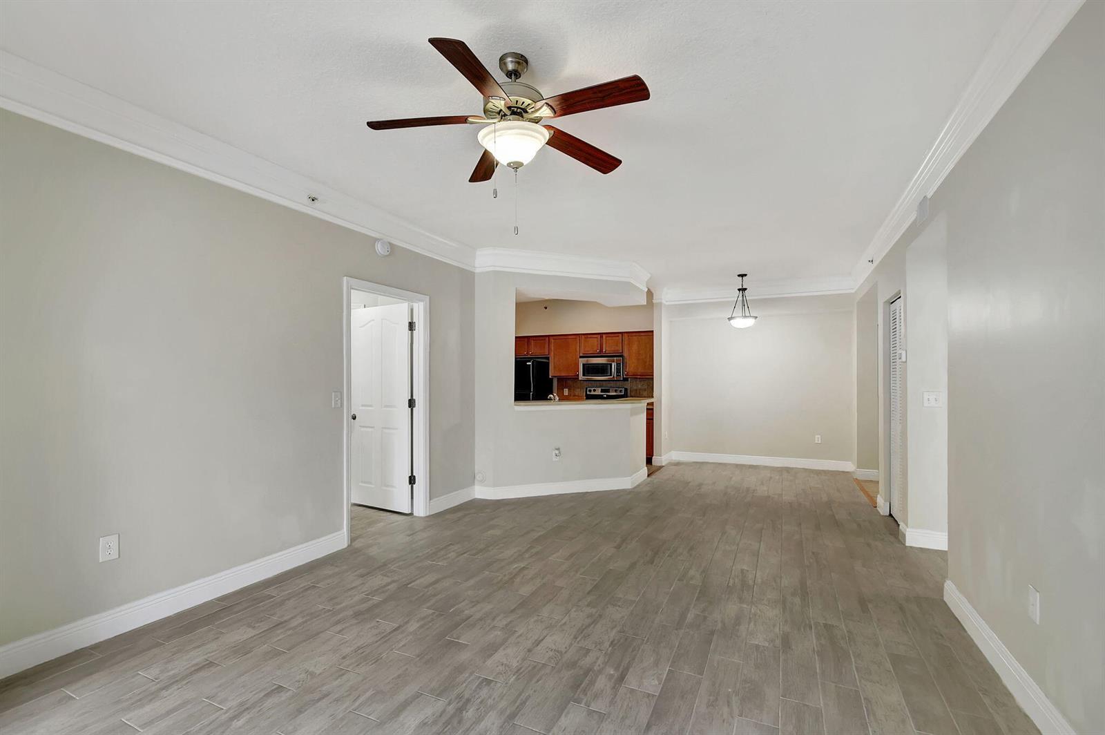 An open living area with gray wood-look tile flooring, a ceiling fan, and a kitchen pass-through — 9849 Baywinds Drive # 8101, West Palm Beach FL 33411, WEST PALM BEACH, FL