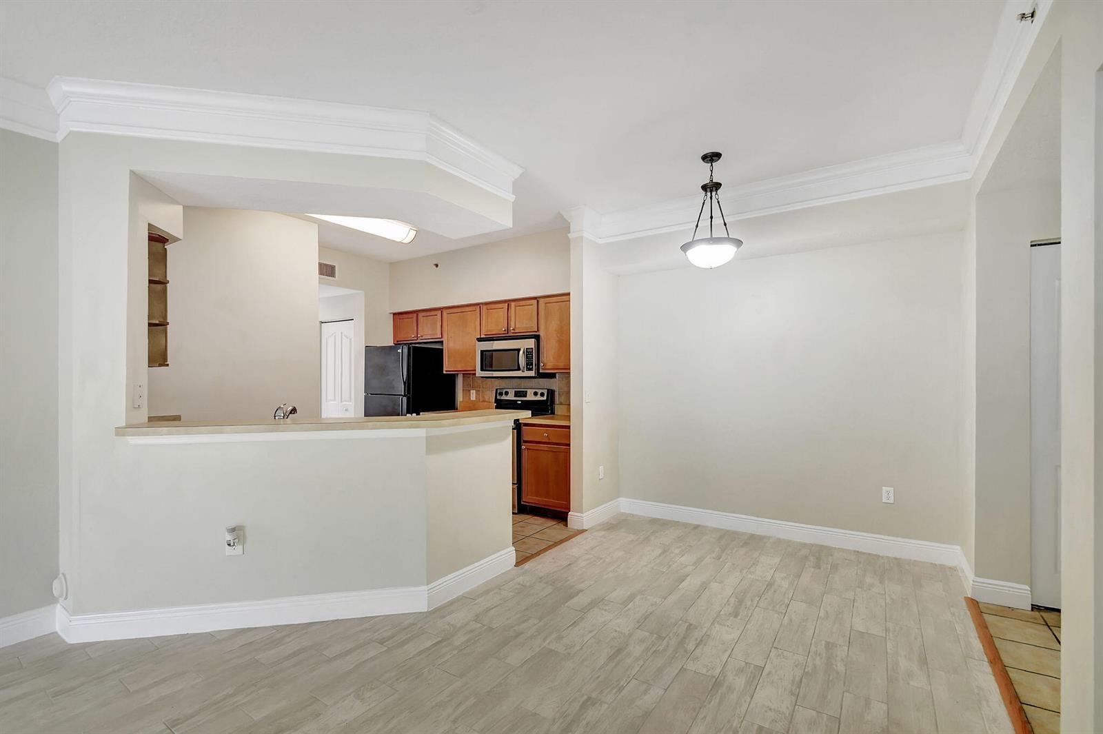 A dining area with wood-look tile floors opens to a kitchen featuring wood cabinetry — 9849 Baywinds Drive # 8101, West Palm Beach FL 33411, WEST PALM BEACH, FL