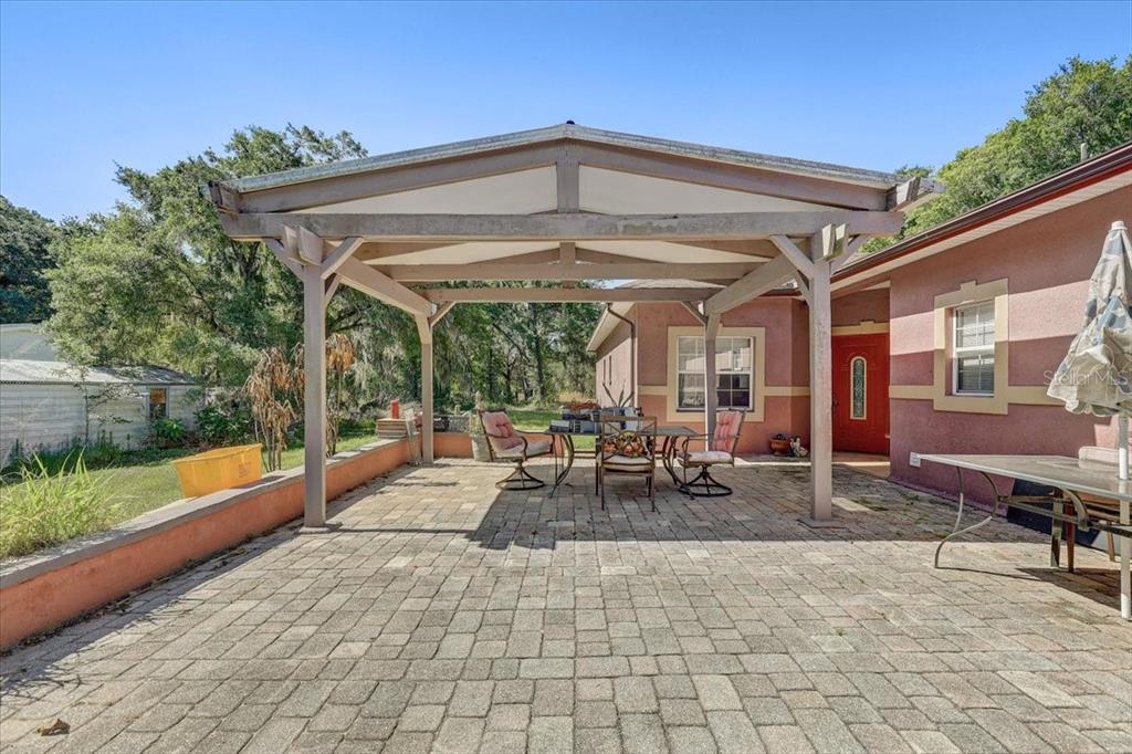 A paved patio features a wooden pergola covering a dining set beside a house exterior — 4954 EWELL ROAD, LAKELAND, FL