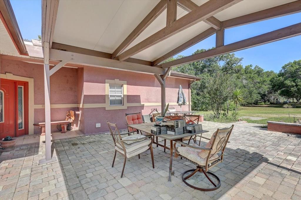 A covered patio with a paved floor, outdoor dining set, and a red exterior wall — 4954 EWELL ROAD, LAKELAND, FL