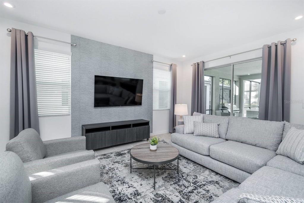 A living room features a gray textured accent wall, a sectional sofa, and a rug — 8937 AMELIA DOWNS TRAIL, KISSIMMEE, FL