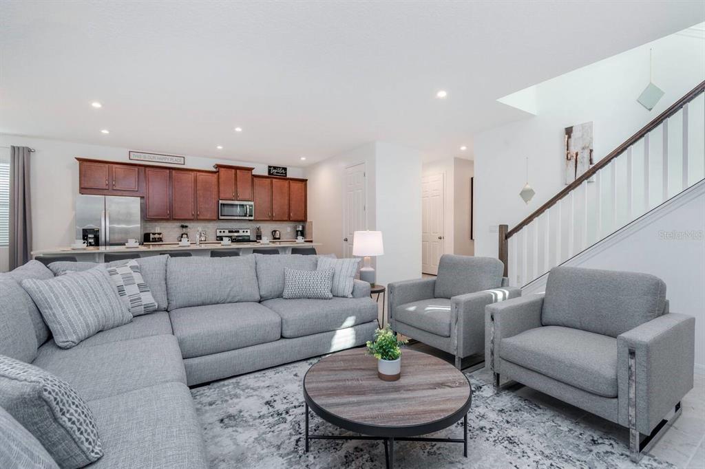 A living room with a grey sectional sofa, two armchairs, and an open kitchen area — 8937 AMELIA DOWNS TRAIL, KISSIMMEE, FL