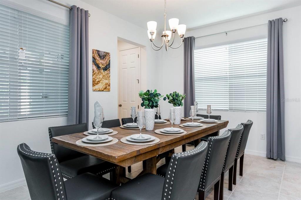 A dining room features a wooden table, black upholstered chairs, and two windows with curtains — 8937 AMELIA DOWNS TRAIL, KISSIMMEE, FL