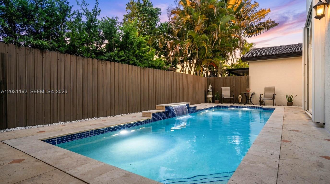 A rectangular swimming pool with a water feature sits in a fenced backyard patio area — 1084 SW 142nd Pl, Miami FL 33184, MIAMI, FL