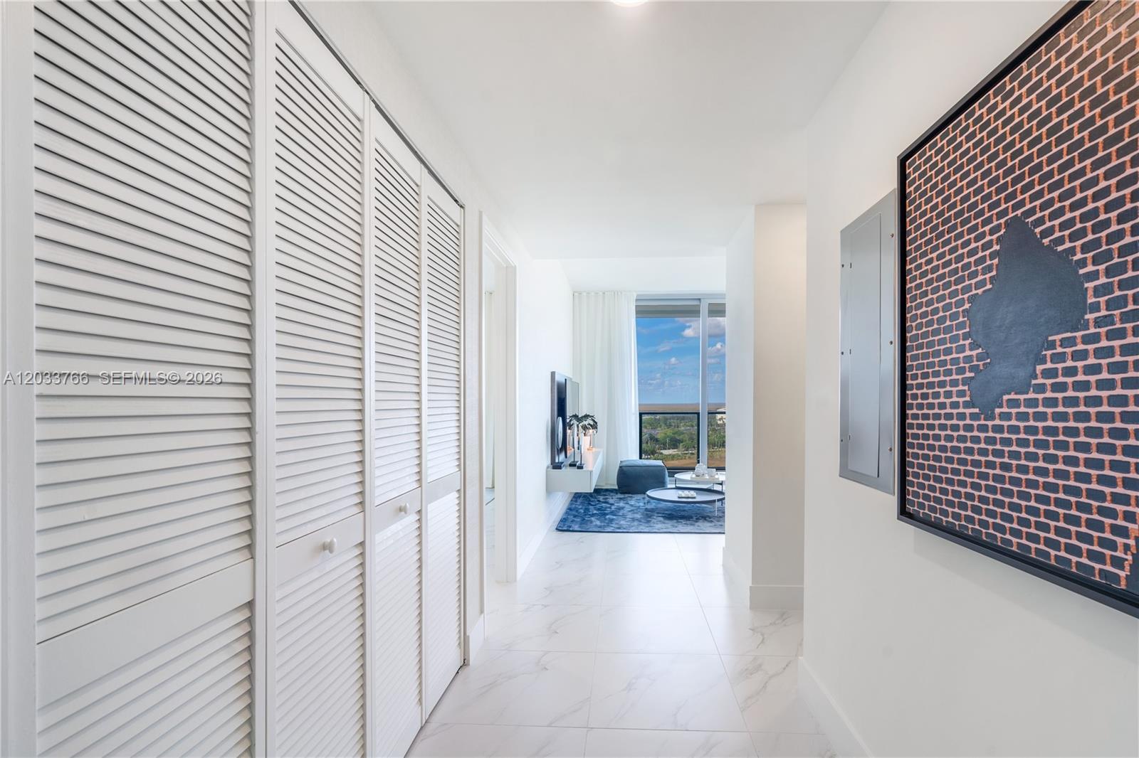 A hallway with white louvered closet doors leads to a living area with floor-to-ceiling windows — 2000 Metropica Way # 1810, Sunrise FL 33323, SUNRISE, FL