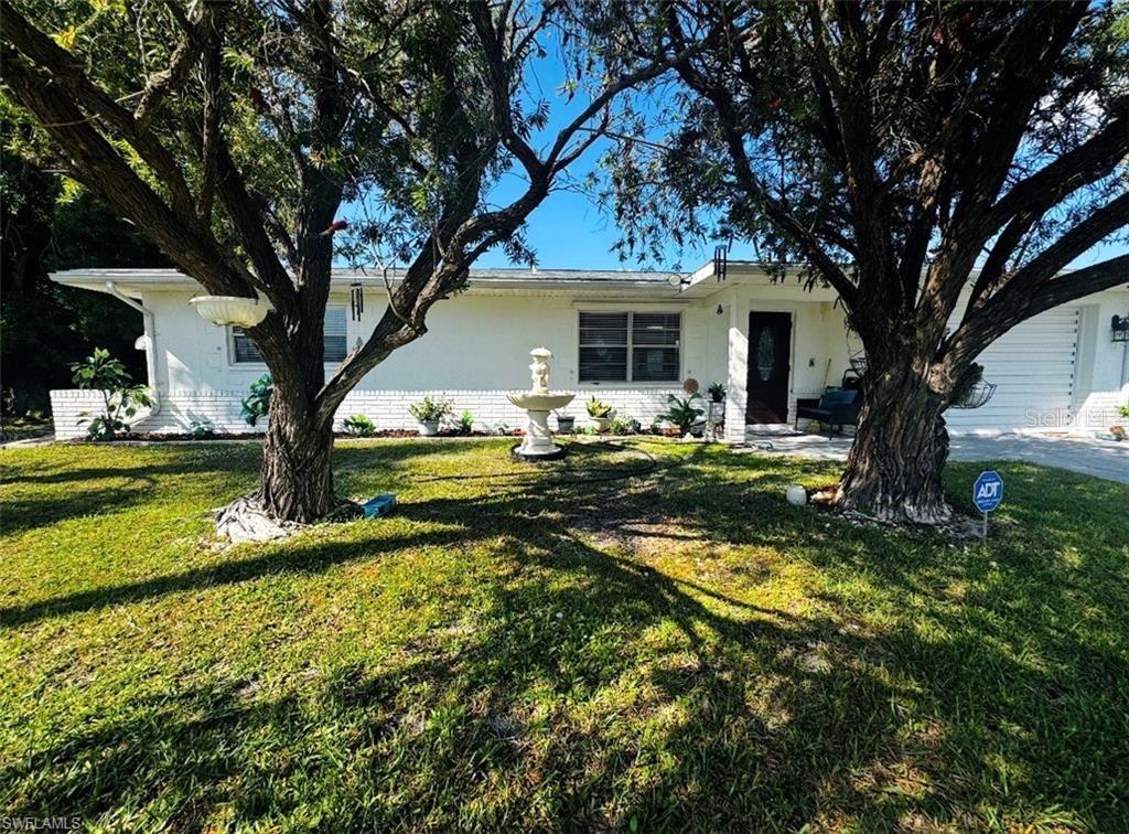 A white single-story house with a front fountain and two large trees in the yard — 710 AQUI ESTA DRIVE, PUNTA GORDA, FL