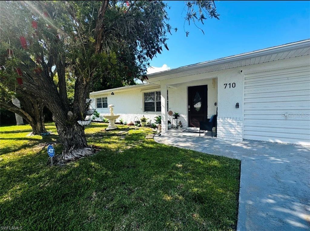 A white brick house with a front porch, a large tree, and a fountain — 710 AQUI ESTA DRIVE, PUNTA GORDA, FL