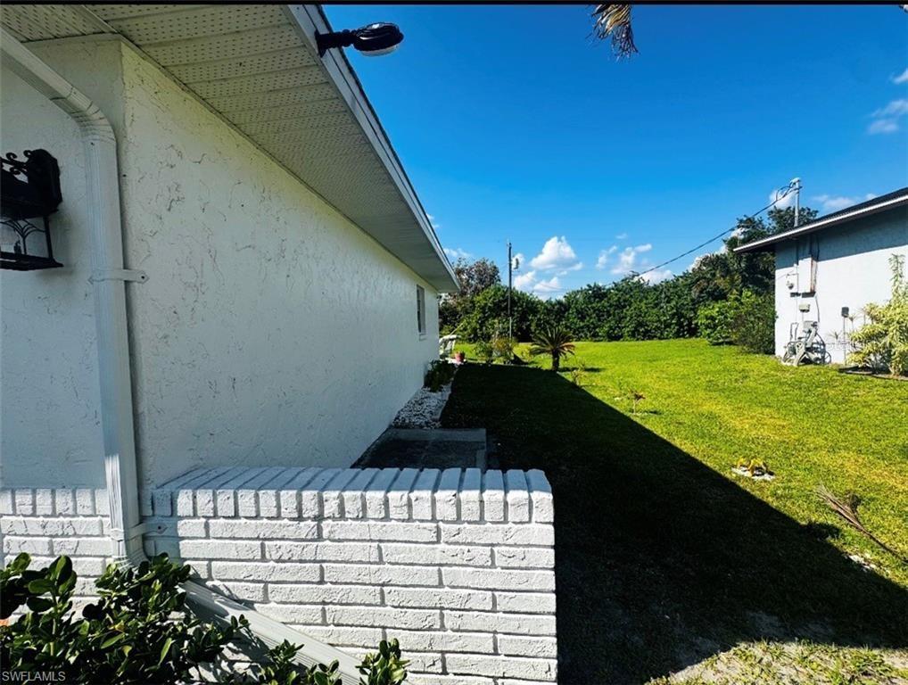 A white brick wall and stucco exterior extend along a grassy side yard — 710 AQUI ESTA DRIVE, PUNTA GORDA, FL