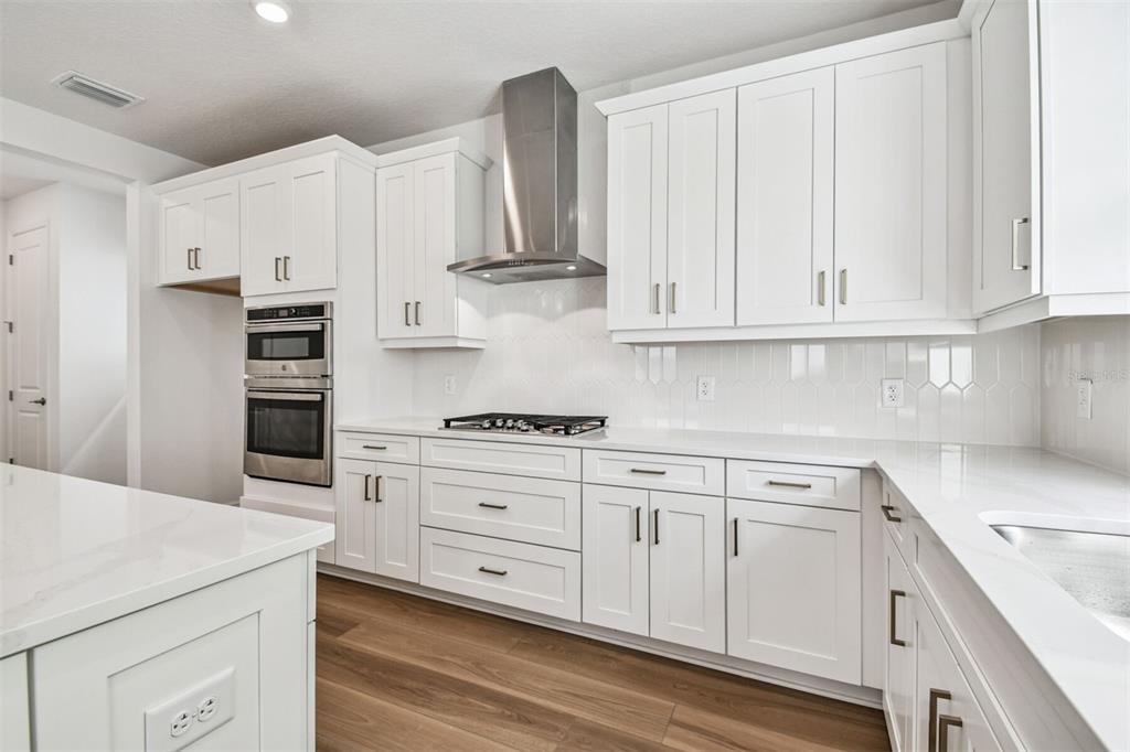 A bright kitchen features white cabinets, a large center island, and wood-look flooring — 7571 HAWKSTONE DRIVE, SARASOTA, FL