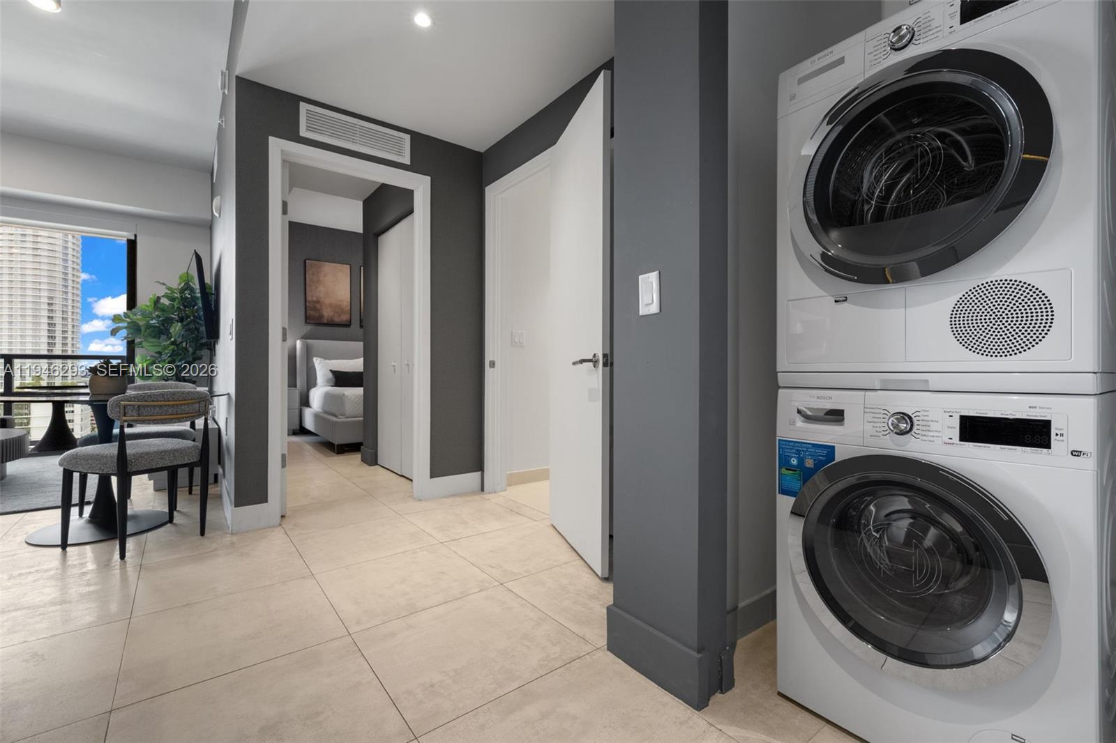 A stacked washer and dryer unit stands in a tiled hallway leading to a bedroom — 239 SW 9th St # 1604, Miami FL 33130, MIAMI, FL
