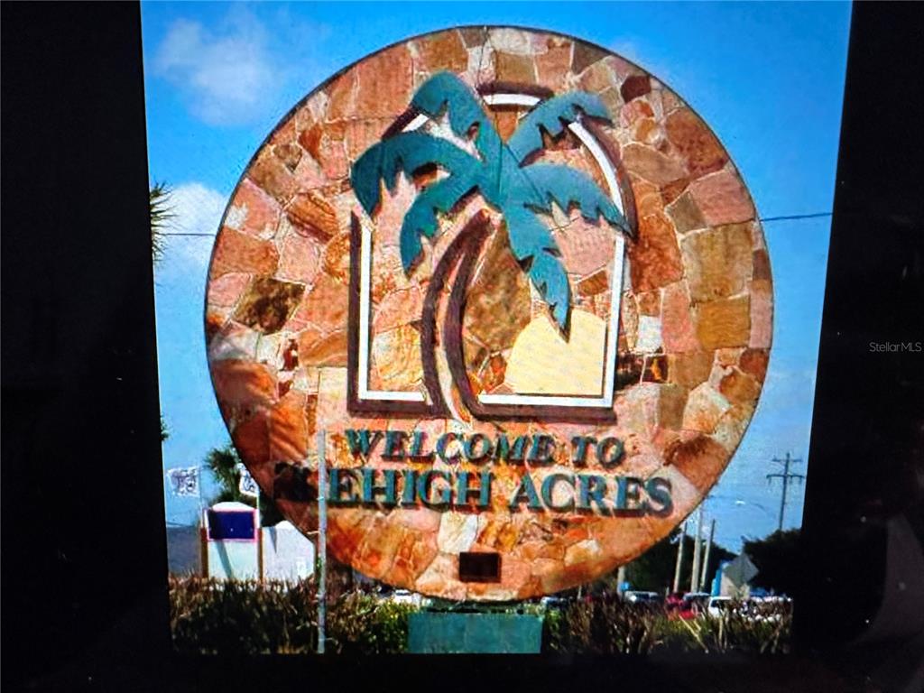 A circular stone sign displays a palm tree graphic and reads Welcome to Lehigh Acres — 2817 56TH STREET W, LEHIGH ACRES, FL
