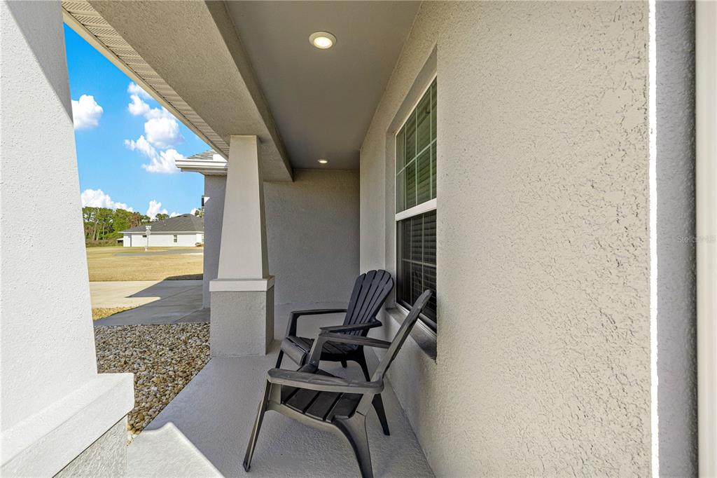 A covered front porch features two black chairs, a stucco wall, and a concrete floor — 4720 SE 89TH PLACE ROAD, OCALA, FL