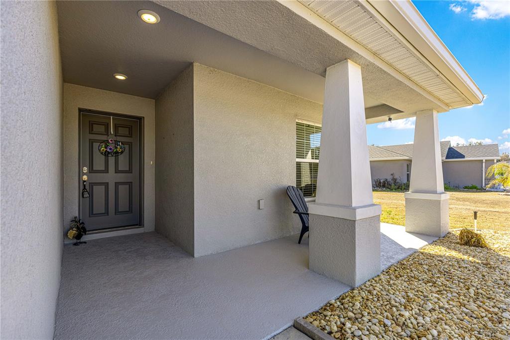 A covered front porch features a gray door, concrete flooring, and two white support columns — 4720 SE 89TH PLACE ROAD, OCALA, FL