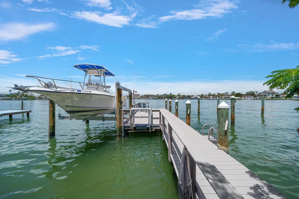 A motorboat sits on a lift at the end of a wooden dock over water — 8405 BAYSHORE DRIVE, TREASURE ISLAND, FL