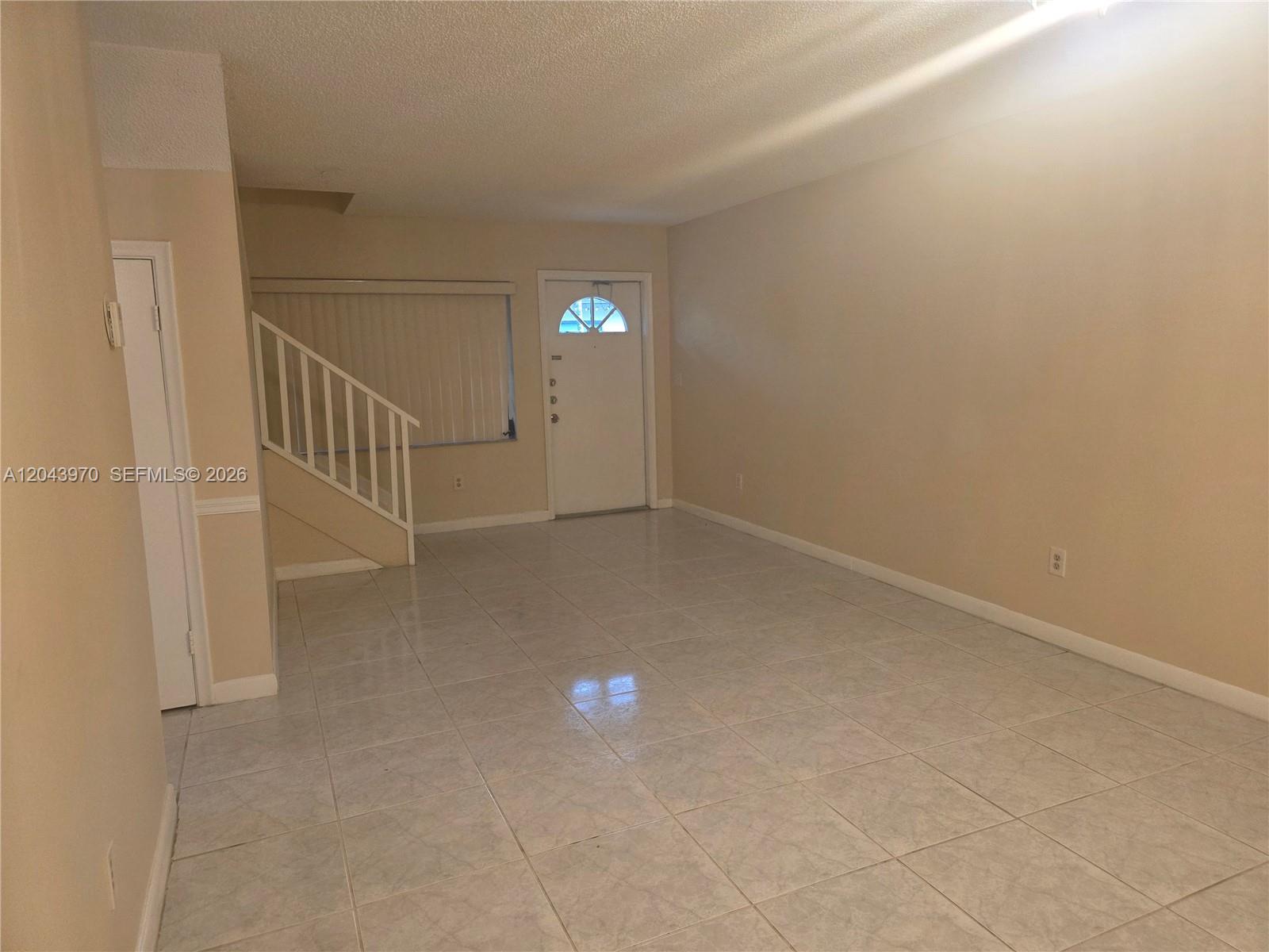 An empty living room features light-colored tile flooring, beige walls, and a staircase with railings — 4586 SW 139th Ct # 763, Miami FL 33175, MIAMI, FL