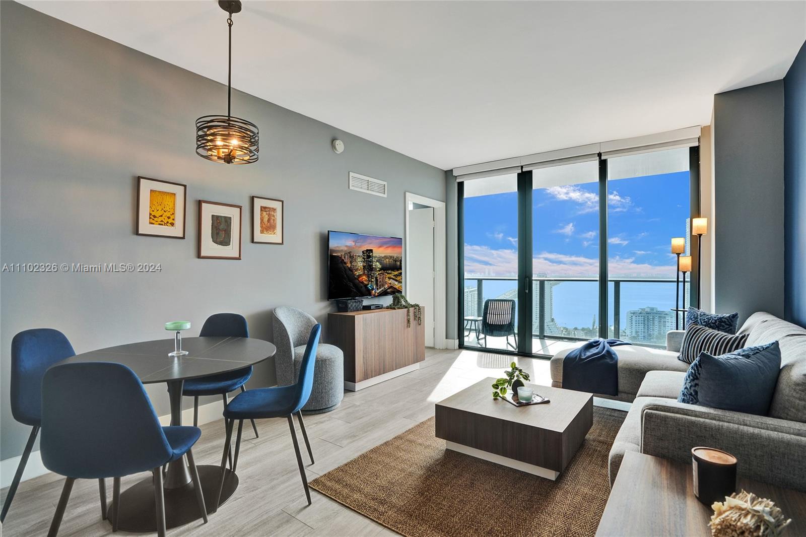 A modern living and dining area features blue chairs, a grey sofa, and floor-to-ceiling windows — 121 NE 34th St # 2906, Miami FL 33137, MIAMI, FL