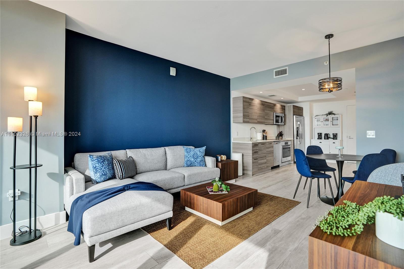 A living room with a navy accent wall, grey sectional sofa, and an open-concept kitchen — 121 NE 34th St # 2906, Miami FL 33137, MIAMI, FL
