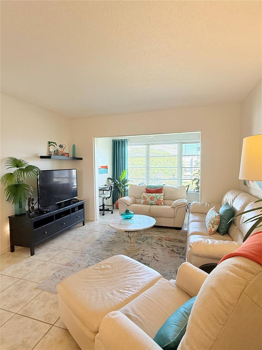 A living room features tile floors, a television on a black stand, and white sofas — 6650 Royal Palm Boulevard # C, Margate FL 33063, MARGATE, FL