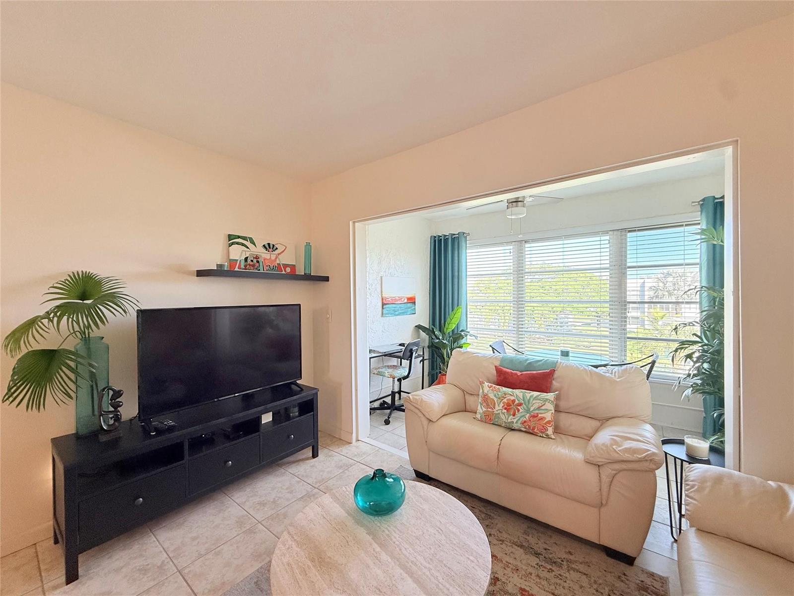 A living room features a black media console, a white sofa, and a sunroom area — 6650 Royal Palm Boulevard # C, Margate FL 33063, MARGATE, FL