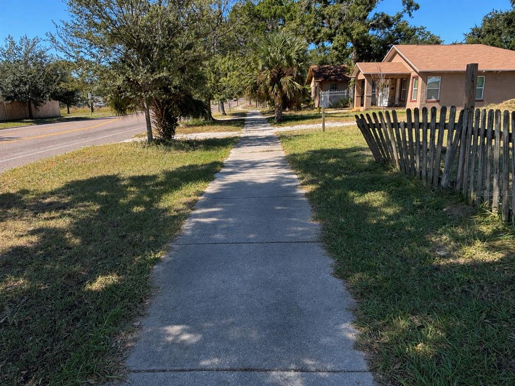 A concrete sidewalk runs between a grassy lawn and a wooden fence near a house — 18TH AVENUE S, ST PETERSBURG, FL