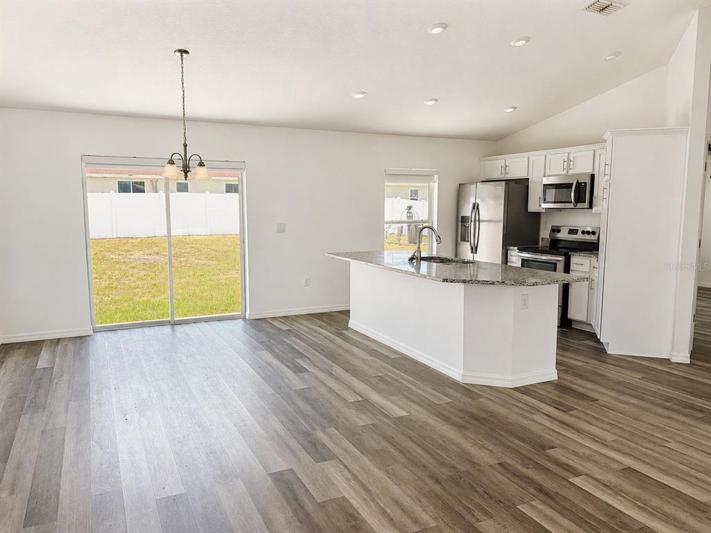 An open-concept kitchen and dining area features white cabinets, granite countertops, and wood-look flooring — 13182 SW 106TH STREET, DUNNELLON, FL