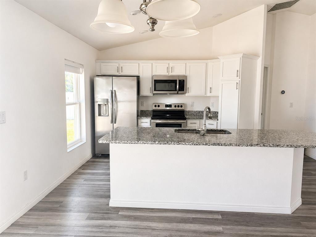 A kitchen features white cabinets, stainless steel appliances, granite countertops, and a central island — 13182 SW 106TH STREET, DUNNELLON, FL