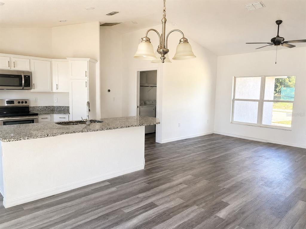 A kitchen with white cabinets and granite countertops opens to a living area with flooring — 13182 SW 106TH STREET, DUNNELLON, FL