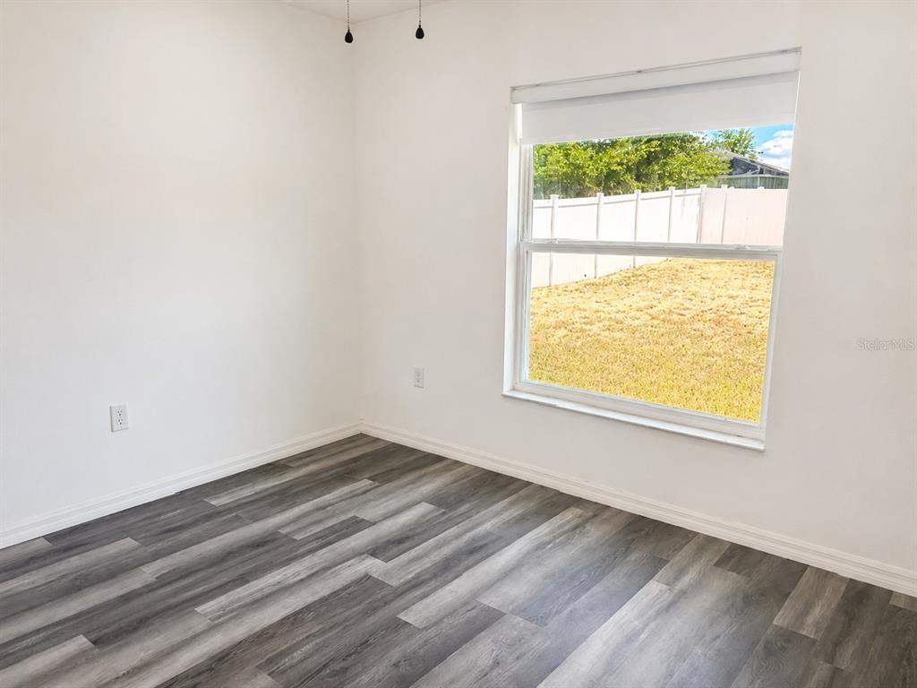 An empty bedroom features white walls, gray wood-look flooring, and a window overlooking a yard — 13182 SW 106TH STREET, DUNNELLON, FL