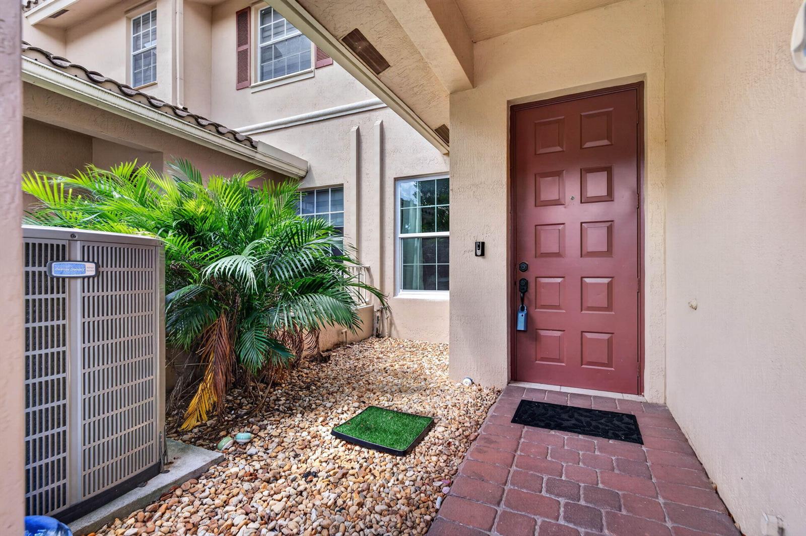 A red front door is situated next to an air conditioning unit and a small palm — 3355 Lakeside Drive, Davie FL 33328, DAVIE, FL