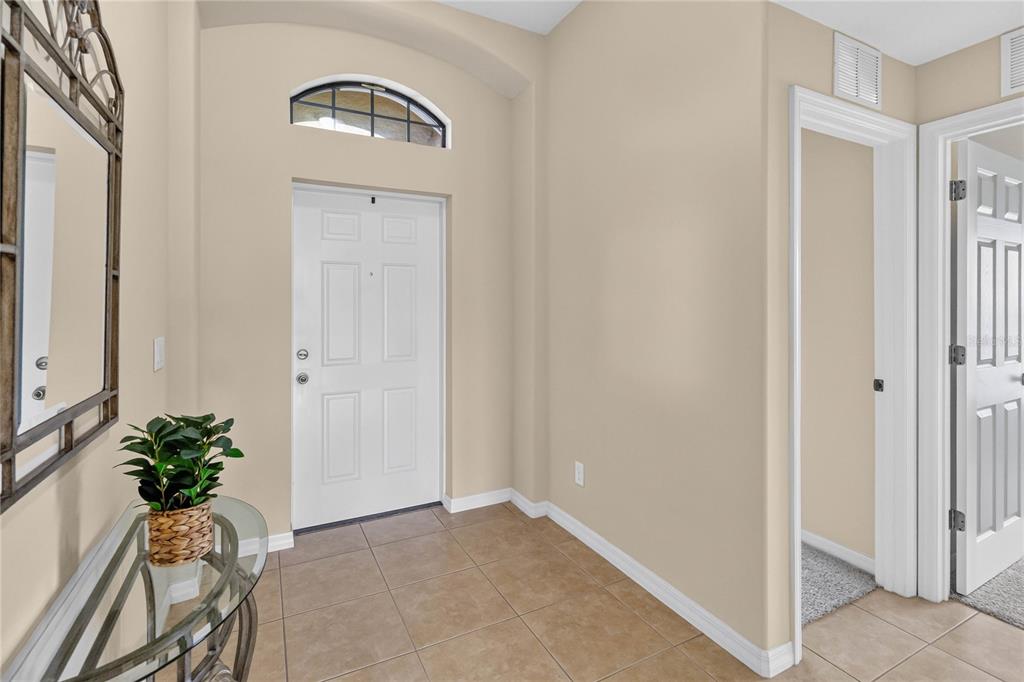 An entryway features a white front door, a glass-topped console table, and tan tile flooring — 3721 MARIETTA WAY, ST CLOUD, FL