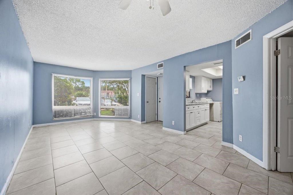 An empty living room with light blue walls, tile flooring, and a view into the kitchen — 2628 LEMON TREE LANE UNIT 6C, ORLANDO, FL