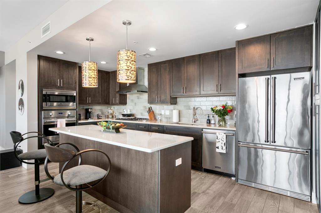 A modern kitchen features dark wood cabinets, a white quartz island, and stainless steel appliances — 176 4TH AVENUE NE UNIT 1002, ST PETERSBURG, FL