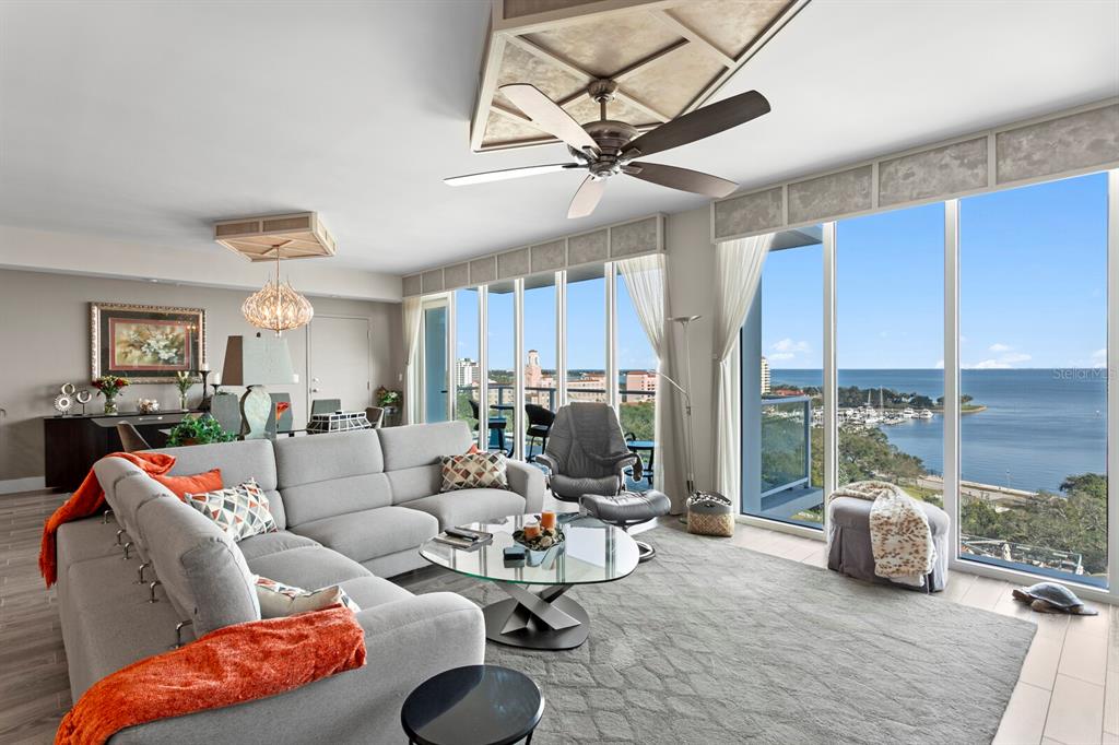 A living room with a gray sectional sofa, glass coffee table, and floor-to-ceiling windows overlooking water — 176 4TH AVENUE NE UNIT 1002, ST PETERSBURG, FL