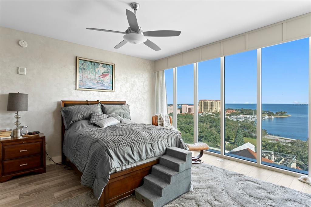 A bedroom features a bed with pet stairs, a ceiling fan, and floor-to-ceiling waterfront windows — 176 4TH AVENUE NE UNIT 1002, ST PETERSBURG, FL