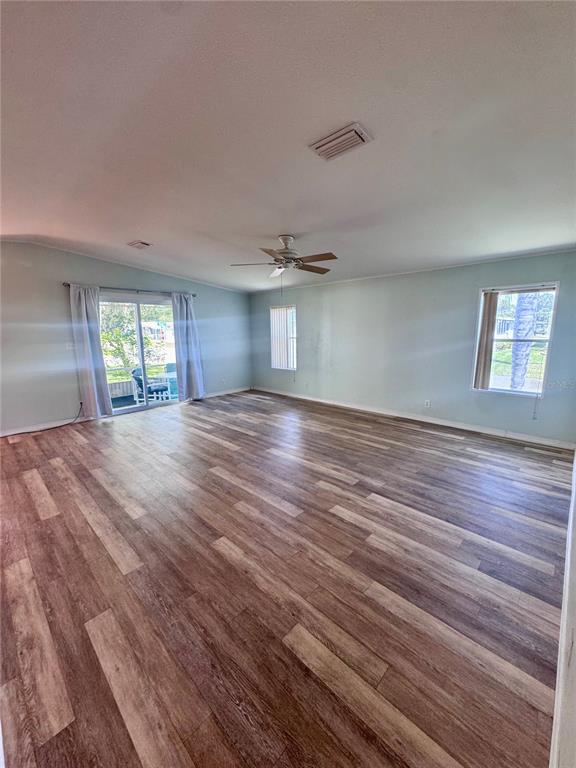 A spacious, empty living room features light-colored walls, wood-look flooring, a ceiling fan, and sliding doors — 4385 MAPLE AVENUE, EDGEWATER, FL