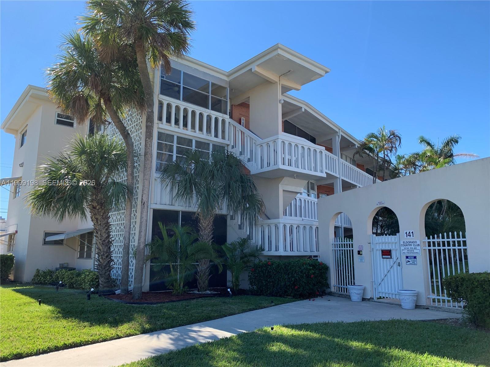A multi-story apartment building with white balconies and a gated entrance under a clear sky — 141 NE 10th Ave # 17B, Hallandale Beach FL 33009, HALLANDALE BEACH, FL