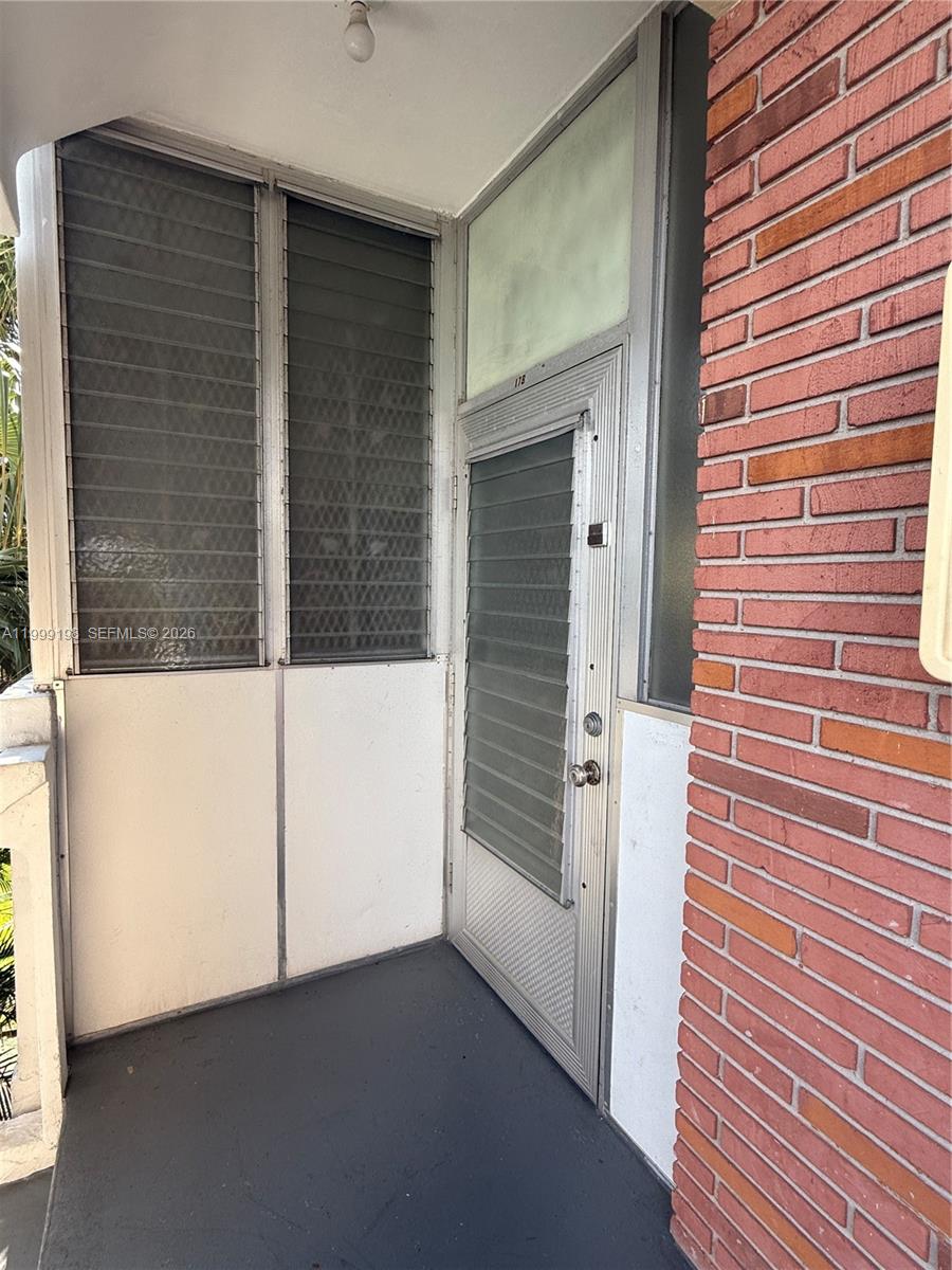A doorway with a louvered screen door sits beside a brick wall on a balcony — 141 NE 10th Ave # 17B, Hallandale Beach FL 33009, HALLANDALE BEACH, FL